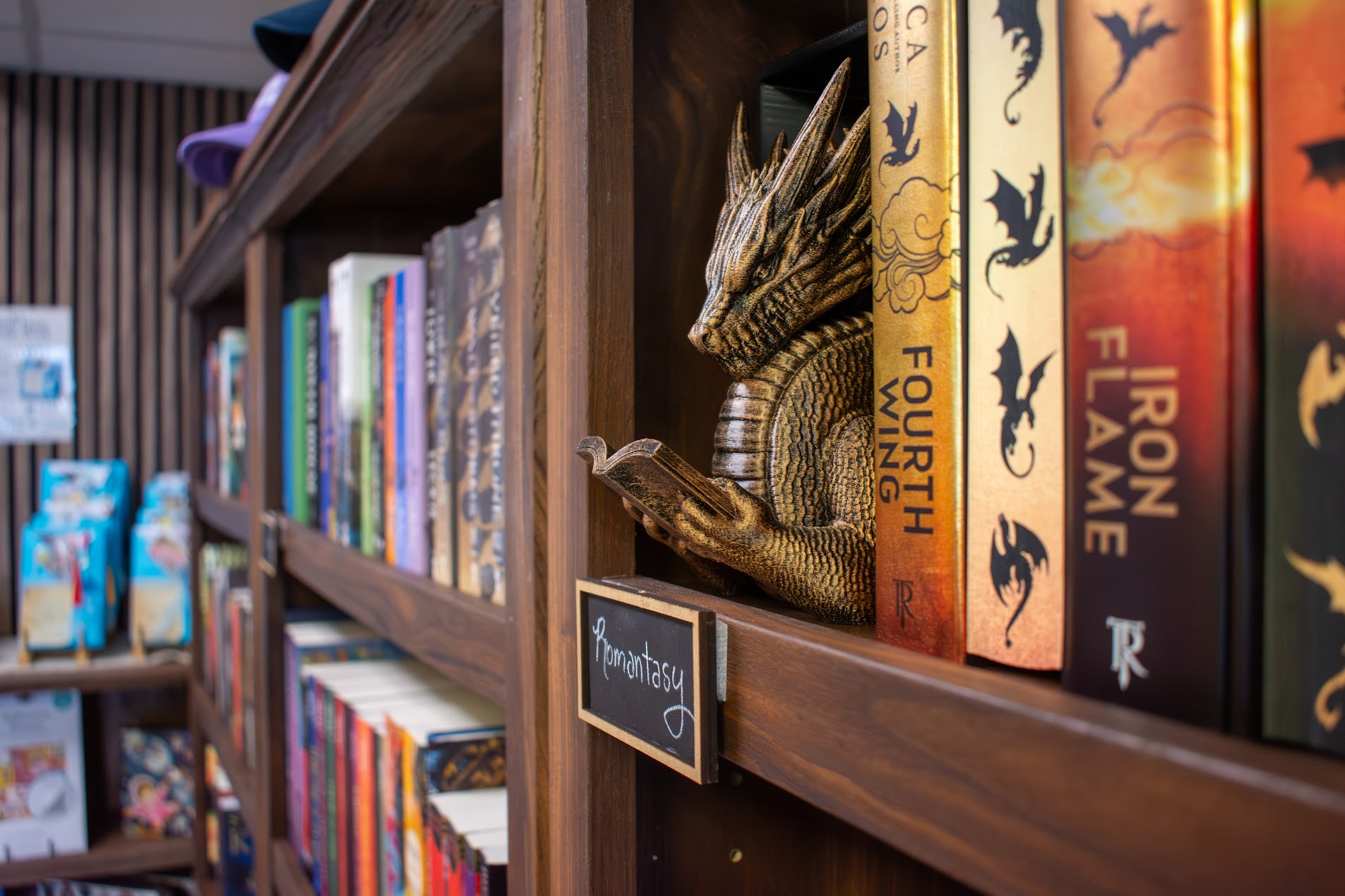 Fantasy books and a decorative dragon on a wooden shelf at Cashmere Books & Gifts.